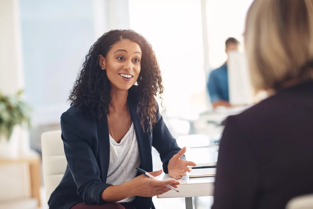 interview with a happy, excited and confident human resources manager talking to a shortlist candidate for a job young business woman meeting with a colleague or coworker in her office at work